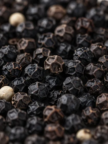Svarte pepperkorn og malt pepper i keramikkskål og på treoverflate